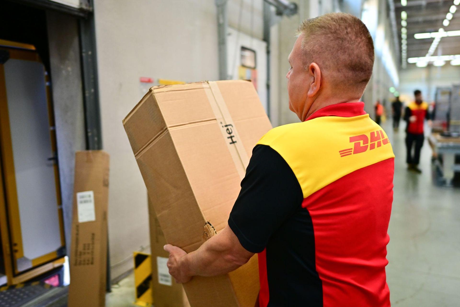Ein Paketbote schleppt in einem DHL-Standort ein schweres Paket. (Archivbild) (Bild: Sebastian Christoph Gollnow/dpa)