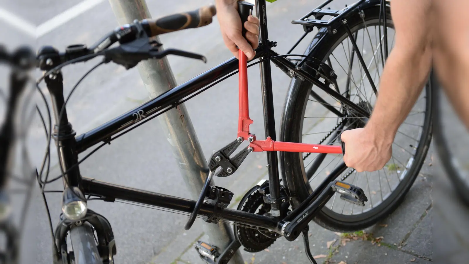 Ein Mann versucht mit einem Bolzenschneider, ein Fahrradschloss aufzubrechen (gestellte Szene). (Bild: Andreas Gebert/dpa)