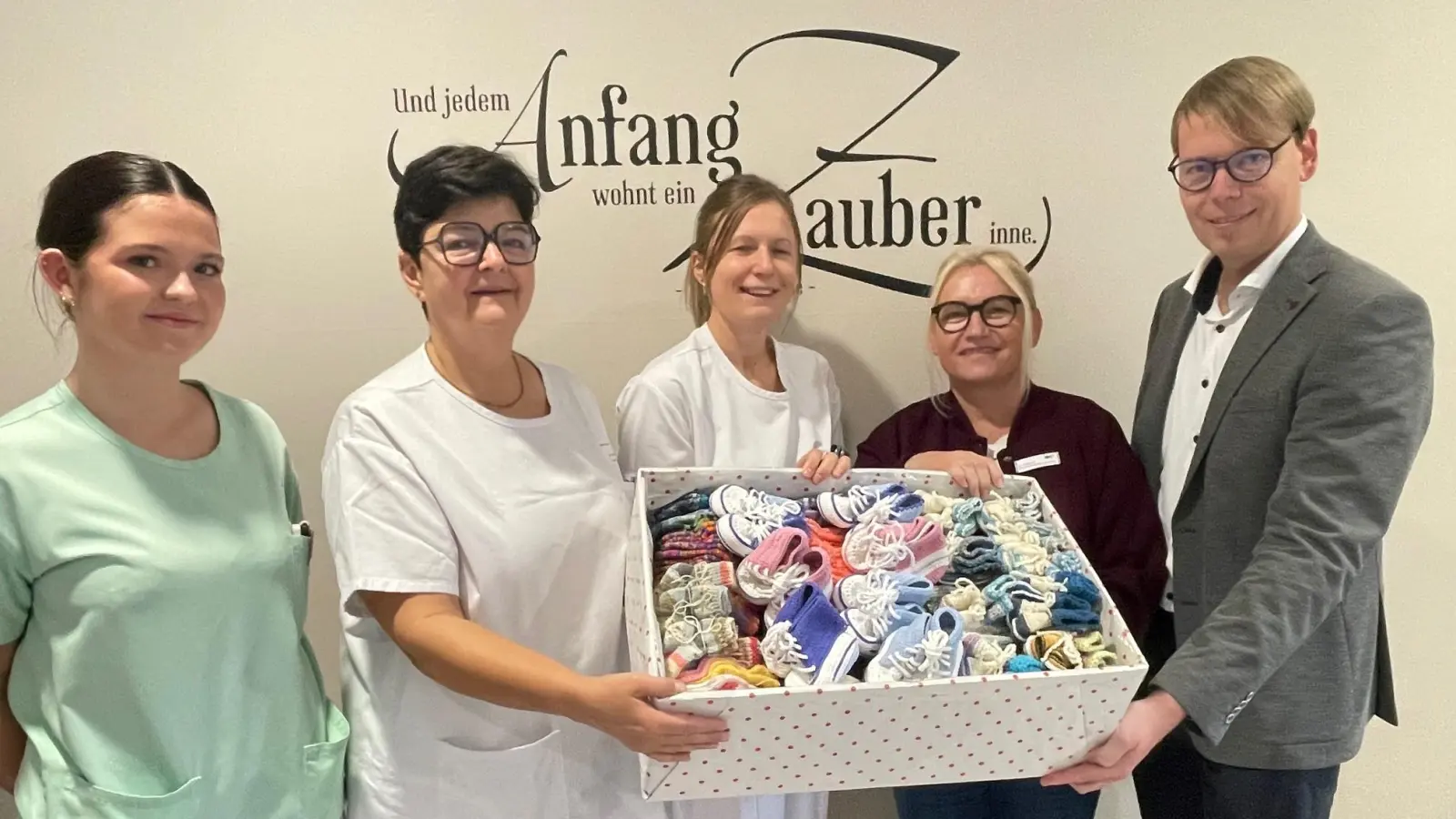 Burgi Zielbauer (Zweite von rechts) überreichte eine Kiste mit 220 Paar gestrickten Söckchen und Schühchen an die Station 32 des Klinikums Weiden. Darüber freuen sich Klinikdirektor Stephan Schumacher (rechts) sowie (von links) Schwesternschülerin Lara Trinkner, stellvertretende Stationsleiterin Jacqueline Kleber und Oberärztin Dr. Ines Erhardt. (Bild: Friedrich Peterhans, KNO)